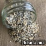 Everything Bagel Spice spilling out of a glass jar, highlighting the abundance and texture of the blend.