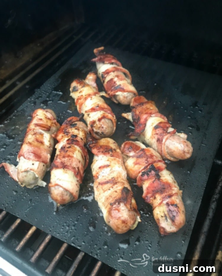 Kraut Stuffed Bacon Wrapped Brats grilling on an outdoor grill