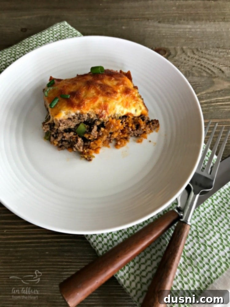 A slice of Mom's Taco Casserole on a plate, showing the layers of Doritos, ground beef, and cheese. It's garnished with fresh cilantro and a lime wedge.