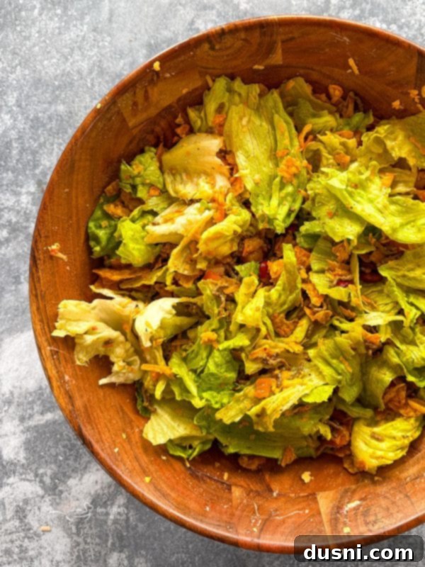 A dish of freshly prepared Taco Salad, featuring crisp lettuce, seasoned ground beef, tomatoes, cheese, and a dollop of sour cream.