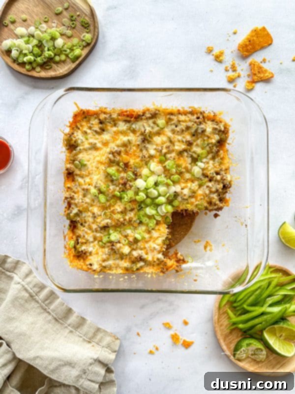 A close-up of a serving of Doritos Taco Casserole on a white plate, showing melted cheese and seasoned meat mixture over a bed of crunchy crushed Doritos. The casserole is bubbling and golden brown.