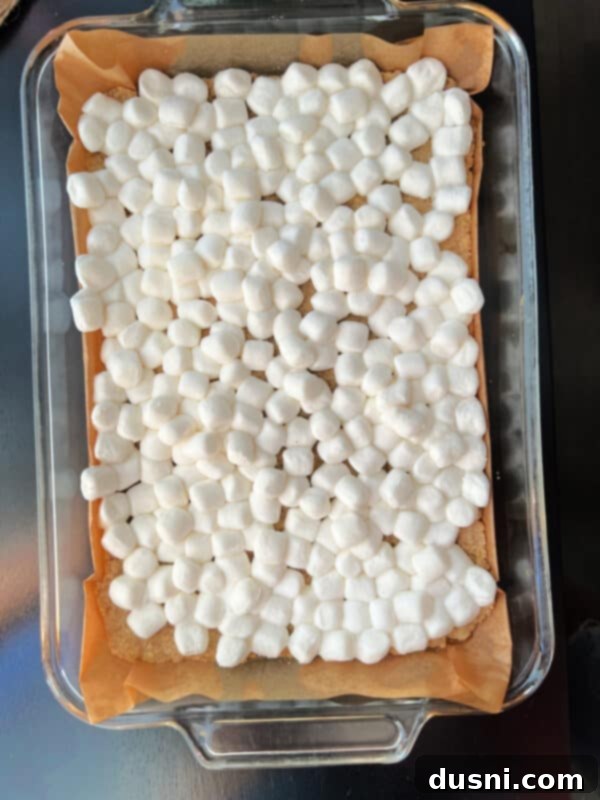 Marshmallows spread over baked crust for Candy Corn Salted Nut Roll Bars