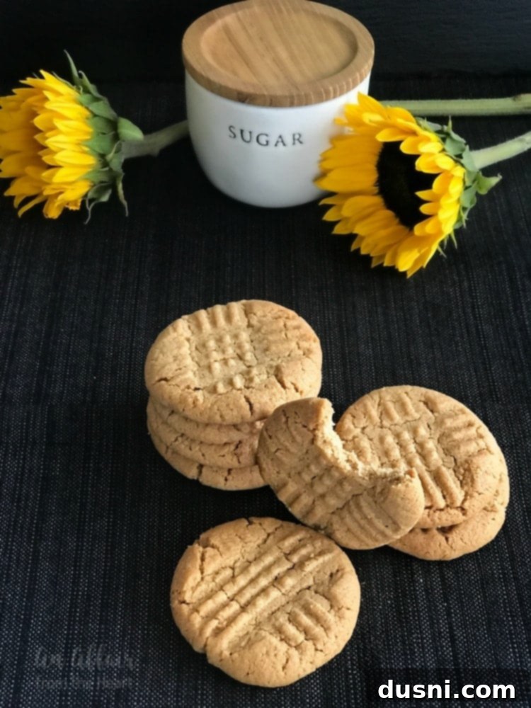 Easy 3-Ingredient Peanut Butter Cookies 9 A hand breaking a freshly baked 3-ingredient peanut butter cookie in half, showing its soft and chewy texture.