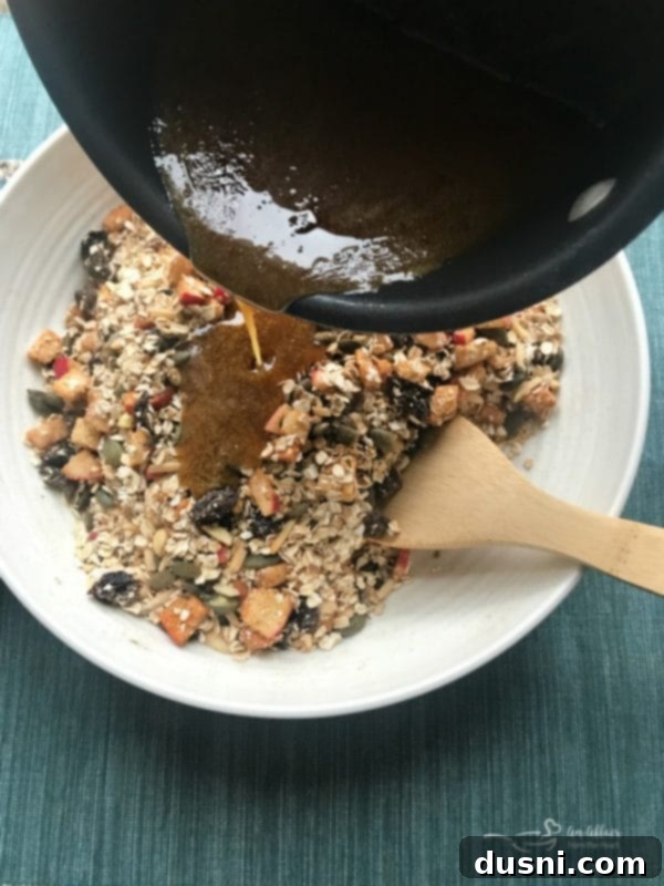 Pouring the warm honey and sugar mixture over Fresh Apple Cinnamon Granola dry ingredients