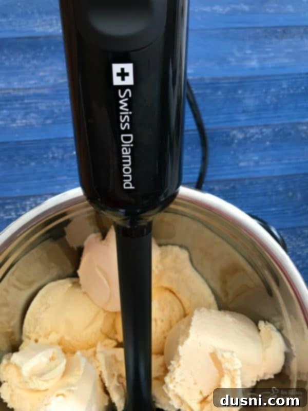 Homemade Dairy Queen Apple Pie Blizzard 12 Hard vanilla ice cream in a stainless steel bowl, being blended with an immersion blender for a smooth blizzard base.