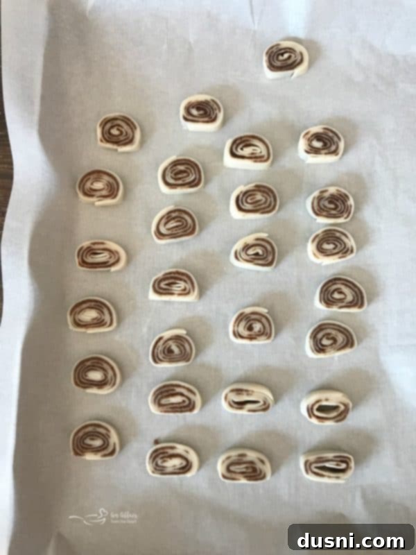 Pumpkin Spice Pie Crust Swirls 7 Sliced pumpkin spice pinwheel cookies arranged on a parchment-lined baking sheet before baking