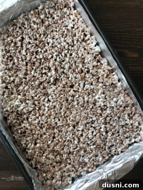 Pressing Cocoa Krispies mixture into a prepared baking pan