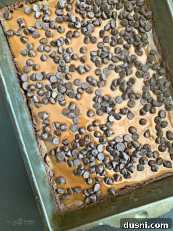 Pouring gooey caramel over the first layer of brownies