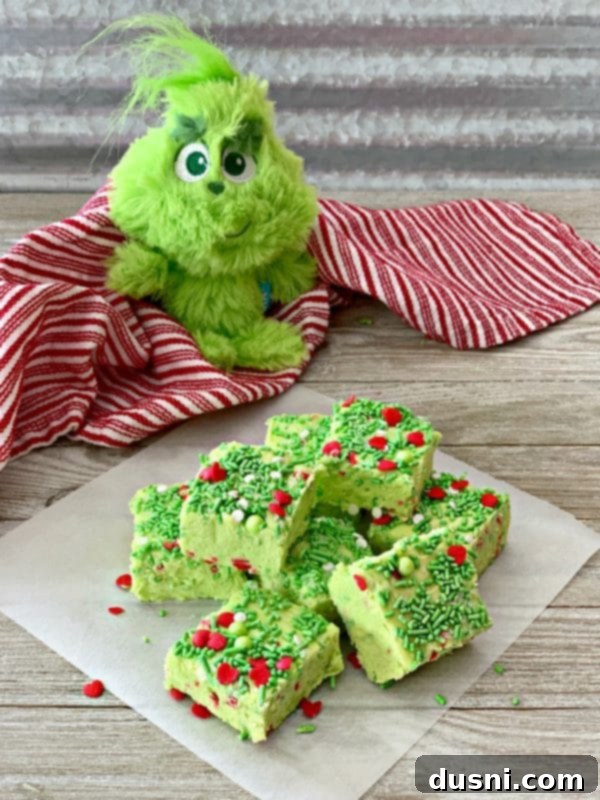 Bright green Grinch Fudge squares topped with colorful sprinkles, arranged neatly on a festive plate.