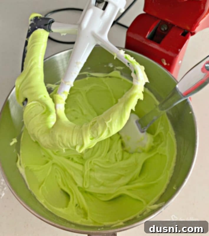 Cream cheese, powdered sugar, and vanilla extract being mixed in a stand mixer bowl for Grinch Fudge.