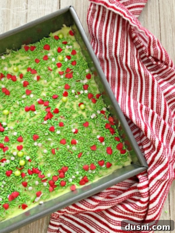 A full 8x8 inch pan of Grinch Fudge, vibrant green and covered in sprinkles, ready to be chilled and cut.