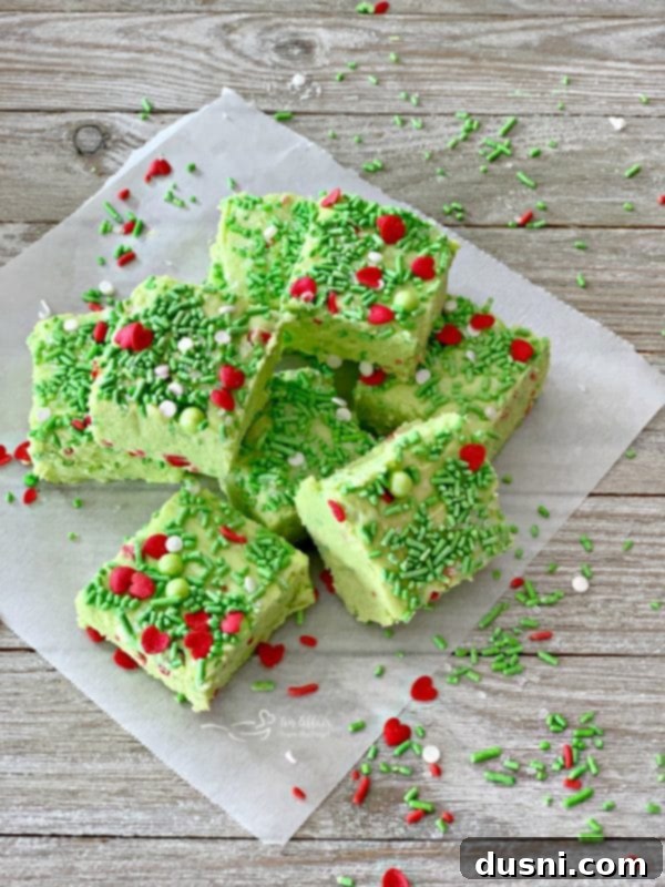 A stack of vibrant Grinch Fudge squares on parchment paper, glistening with sprinkles, ready to be enjoyed.