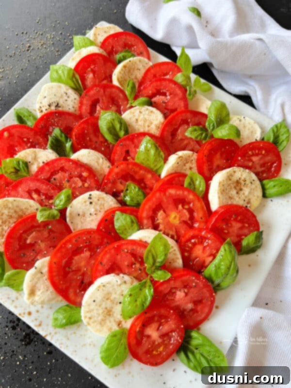 A beautifully arranged Caprese salad with alternating slices of red tomato and white mozzarella, garnished with green basil leaves.