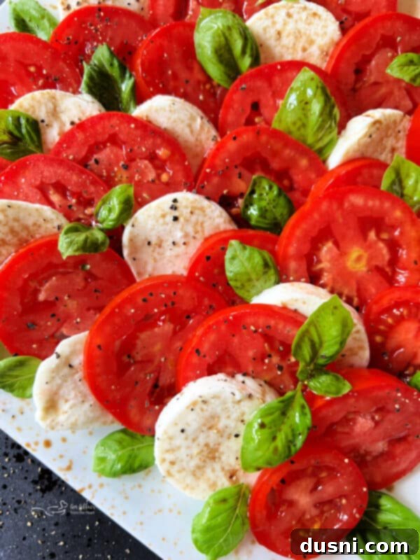 Close-up of fresh basil leaves, red tomatoes, and white mozzarella slices, the essential ingredients for Caprese salad.