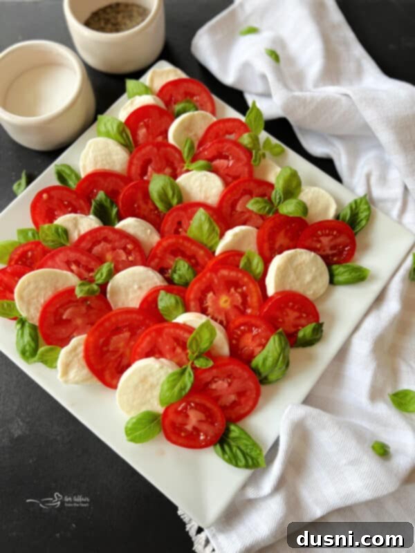 Slices of tomato, mozzarella, and basil leaves artfully arranged in an overlapping pattern on a white serving platter.
