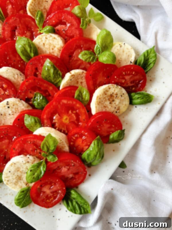 Balsamic glaze being drizzled artfully over a Caprese salad on a white plate, adding a finishing touch.