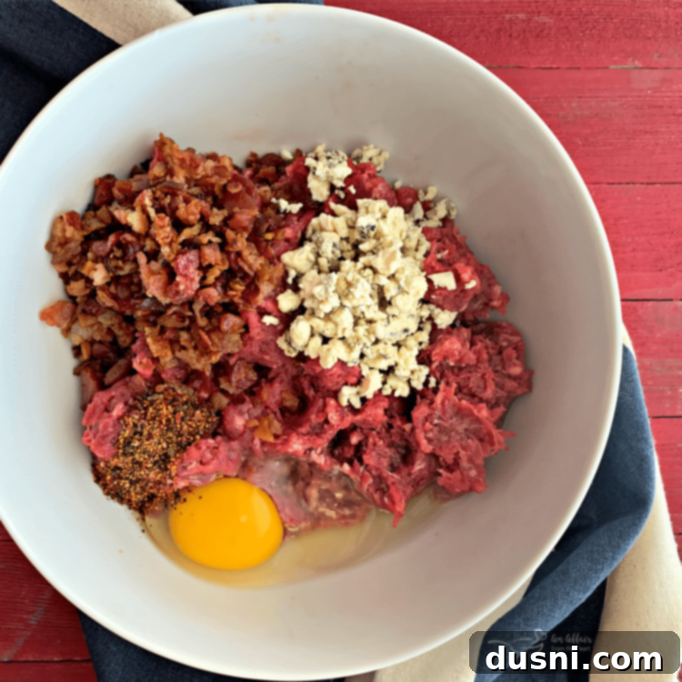 A bowl containing ground beef, crumbled bacon, and bleu cheese, ready to be mixed into burger patties.