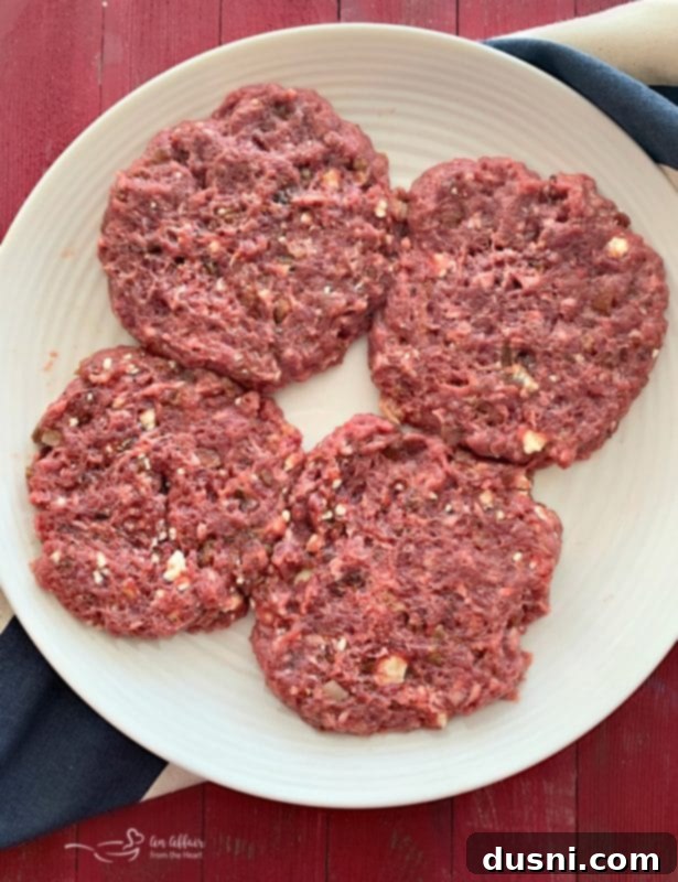 Four hand-formed Red, White & Bleu Burger patties showcasing visible chunks of bleu cheese and bacon before grilling.