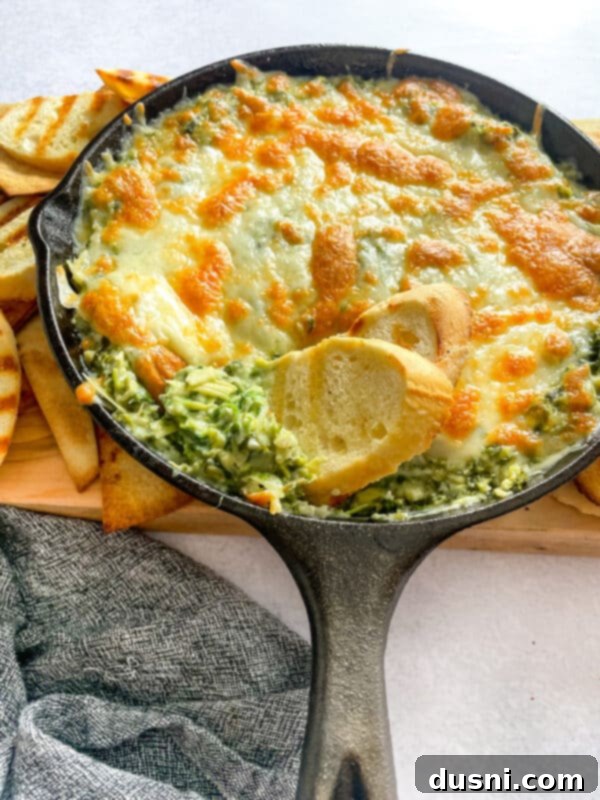 A baking dish filled with spinach artichoke dip, with a serving spoon nestled inside, ready for guests.