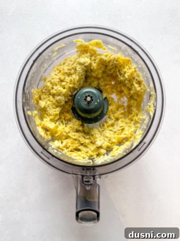 A step-by-step image showing chopped artichoke hearts and garlic in a food processor, ready to be blended.