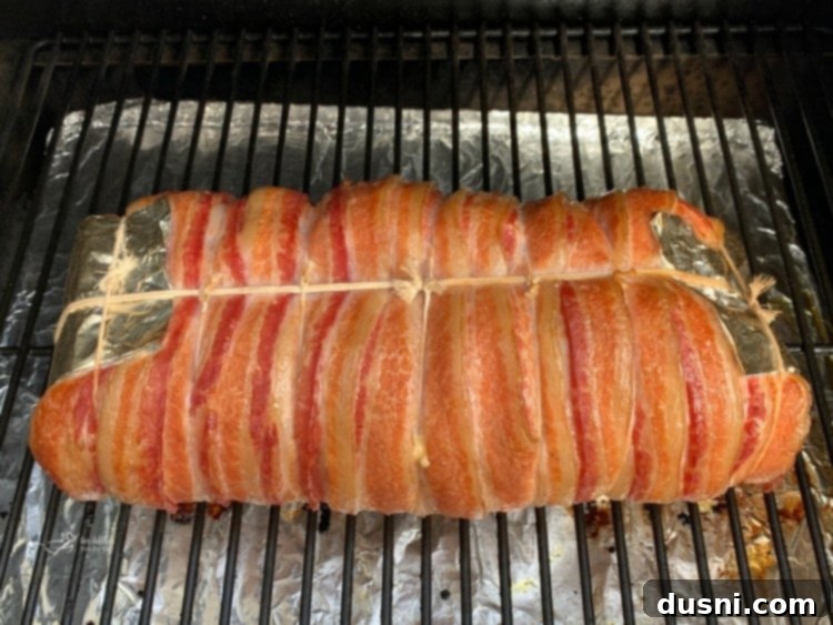 Pastırmalı Lahana Turşusu Dolgulu Domuz Kontrafile 13 Bacon-wrapped pork loin smoking on the grill, showing the golden-brown bacon.