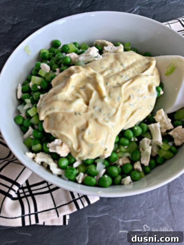 The creamy dill dressing being poured over the vegetables in the mixing bowl.