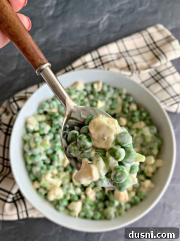 A spoonful of Pea Salad with Cauliflower being lifted from a white bowl.
