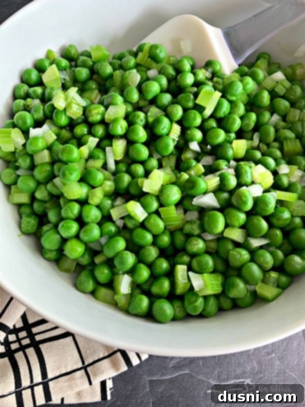 Blanched peas, onion, and celery in a white mixing bowl.