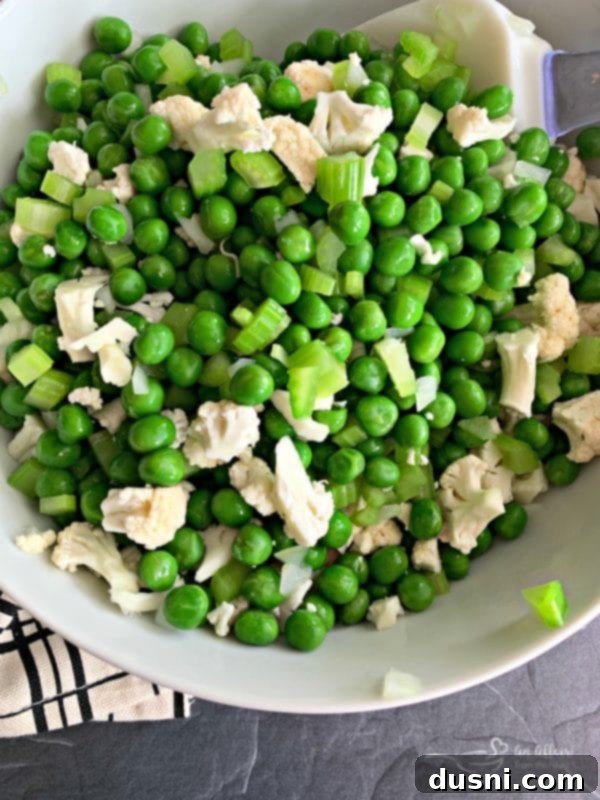 Chopped cauliflower being added to the bowl of blanched peas, onion, and celery.