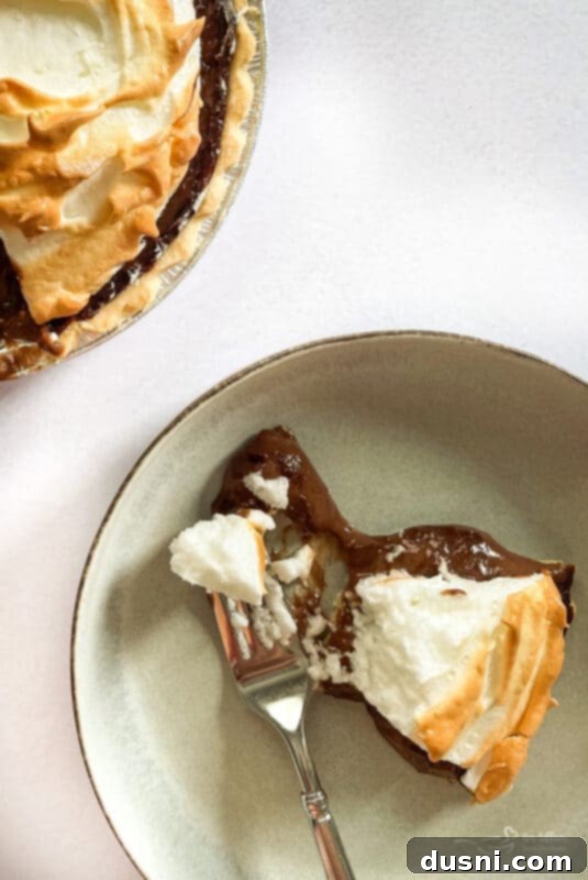 A perfectly portioned slice of chocolate meringue pie on a cream plate with a fork, ready to be enjoyed.
