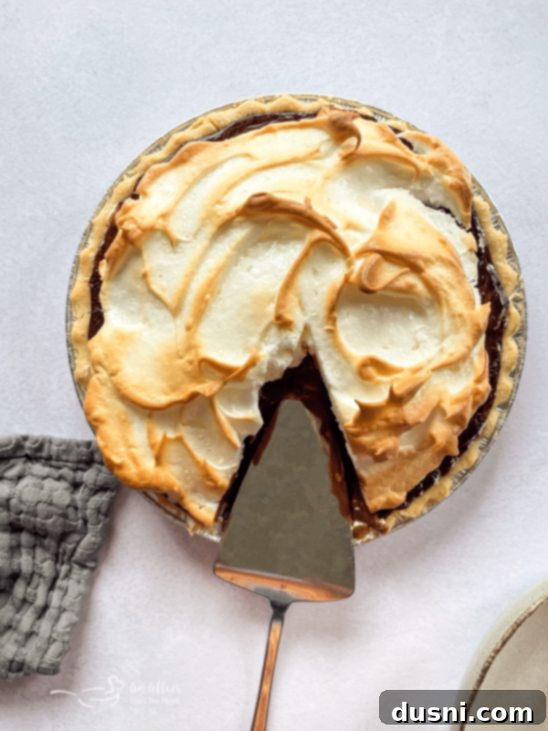 A slice of chocolate meringue pie showing the distinct layers of crust, chocolate custard, and fluffy meringue.