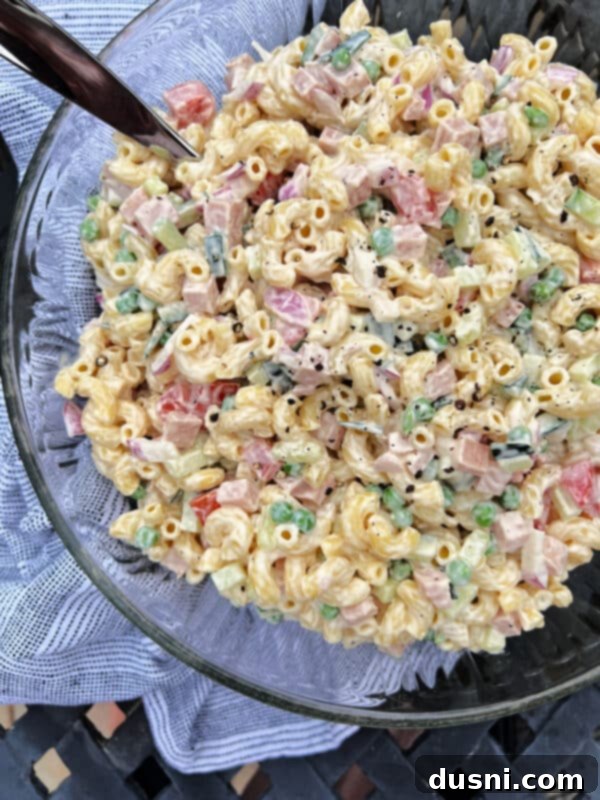 Close-up of creamy Spam pasta salad in a clear glass bowl, garnished with fresh dill.
