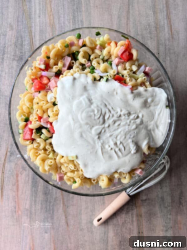 Diced Spam and fresh vegetables being added to cooked elbow macaroni in a large mixing bowl.