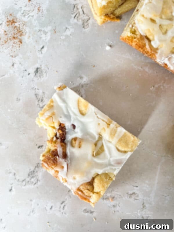 Glazed Snickerdoodle Bars 3 Close-up of freshly baked Iced Snickerdoodle Bars drizzled with vanilla glaze, on a white plate.