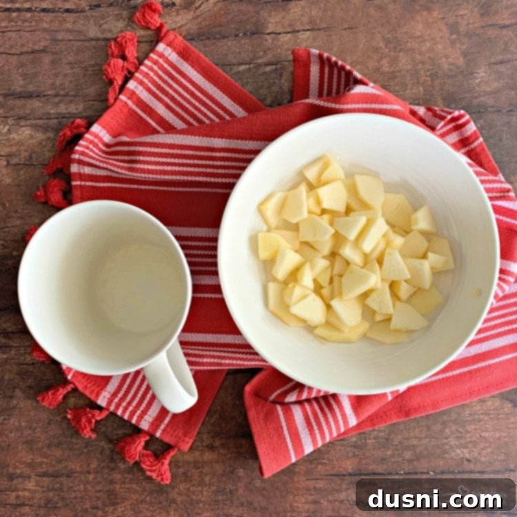 Mug coated with non-stick spray, with peeled and diced apples in a bowl