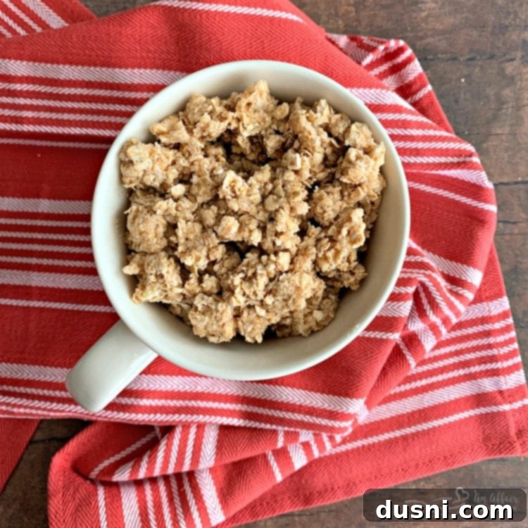 Oatmeal crumb topping layered over the apples in the mug, looking quite full before cooking