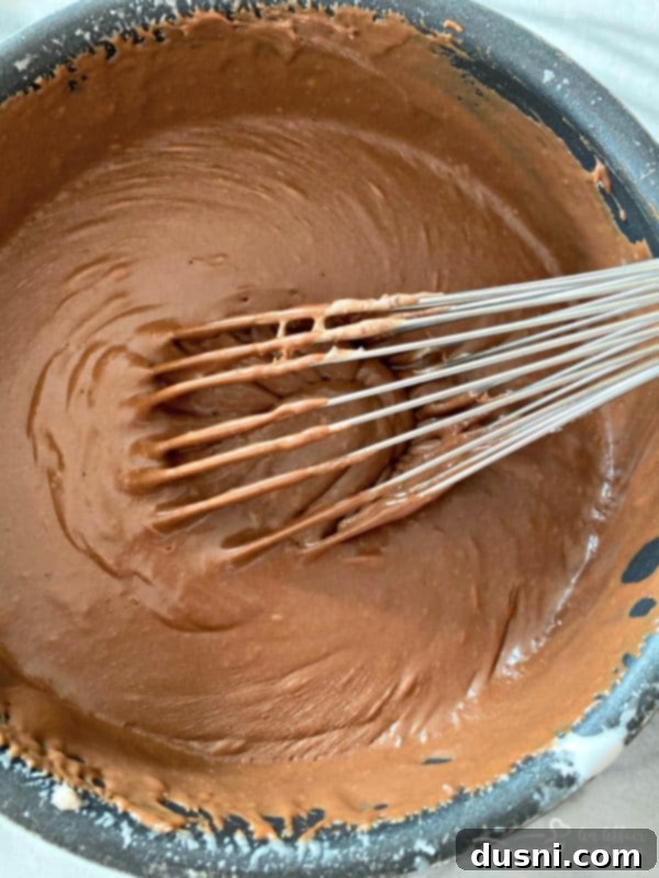 Smooth chocolate fudge being stirred in a saucepan before pouring into the prepared pan.