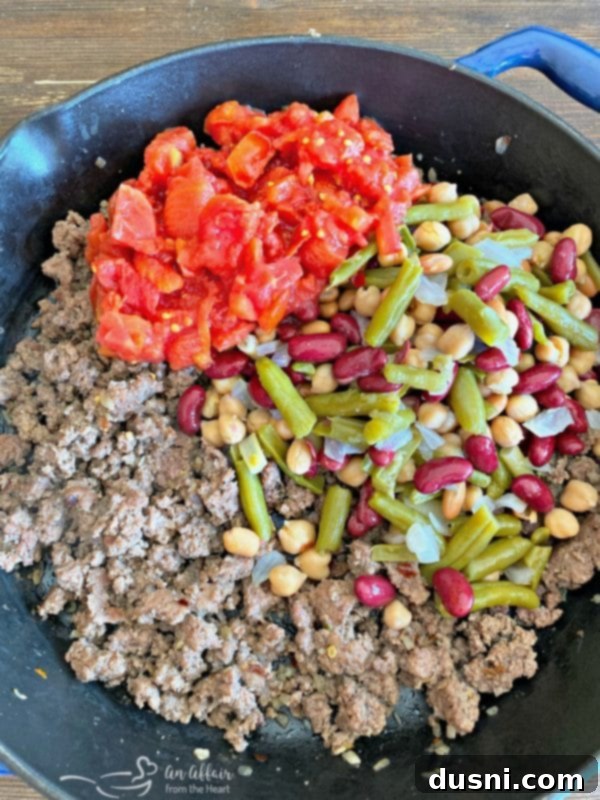 Preparing the five bean beef and noodle casserole by adding beans and tomatoes