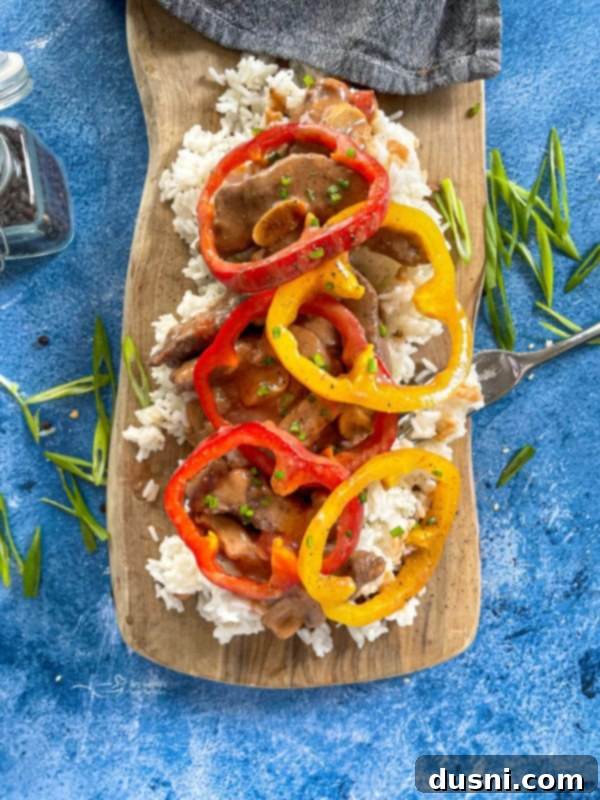 Hearty Pepper Steak served with fluffy white rice and colorful bell peppers on a rustic wooden surface, ready to be enjoyed.