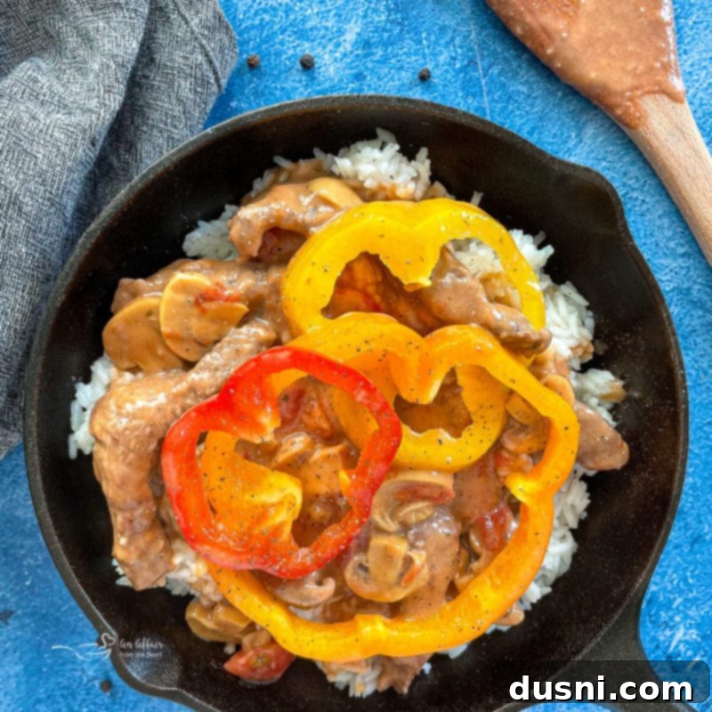 Colorful bell peppers freshly added to the simmering pepper steak in the pan, waiting to be covered and cooked until tender-crisp.