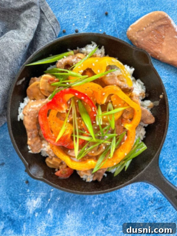 Top-down view of tender beef slices and colorful bell peppers simmering in a rich, savory sauce in a large pan, cooking to perfection.