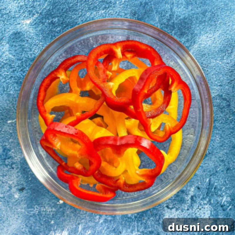 A vibrant bowl filled with sliced red, green, and yellow bell peppers, ready to be added to the pepper steak recipe.