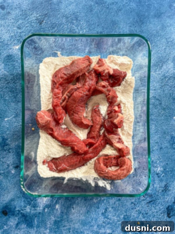 Slices of beef being seasoned with flour, salt, and pepper before cooking.