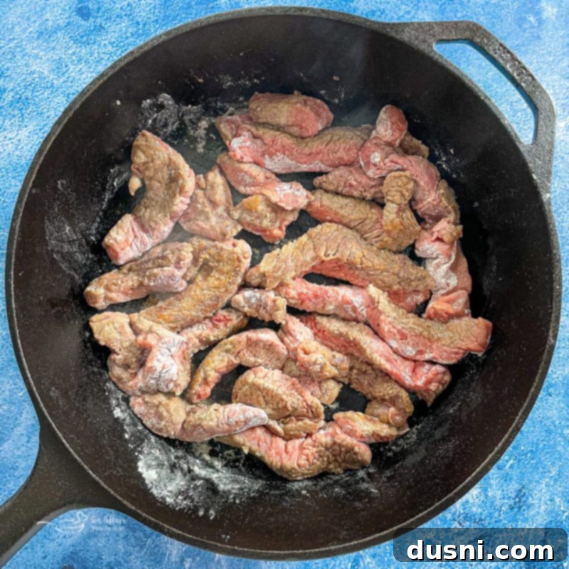 Close-up of minute steak browning in a hot pan with oil, developing a delicious crust.