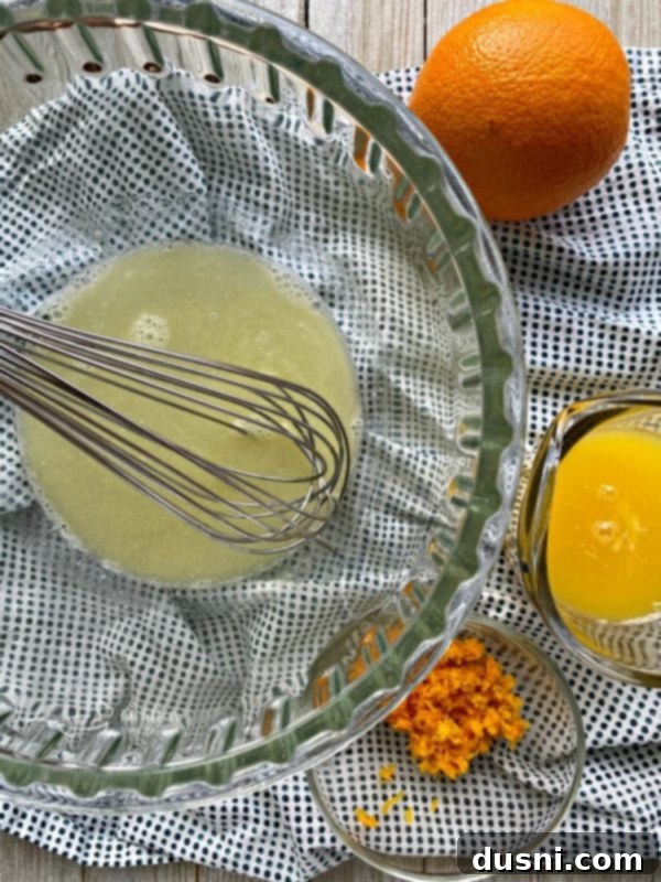 Melted butter combined with boiling water, orange juice, and orange zest in a glass mixing bowl.