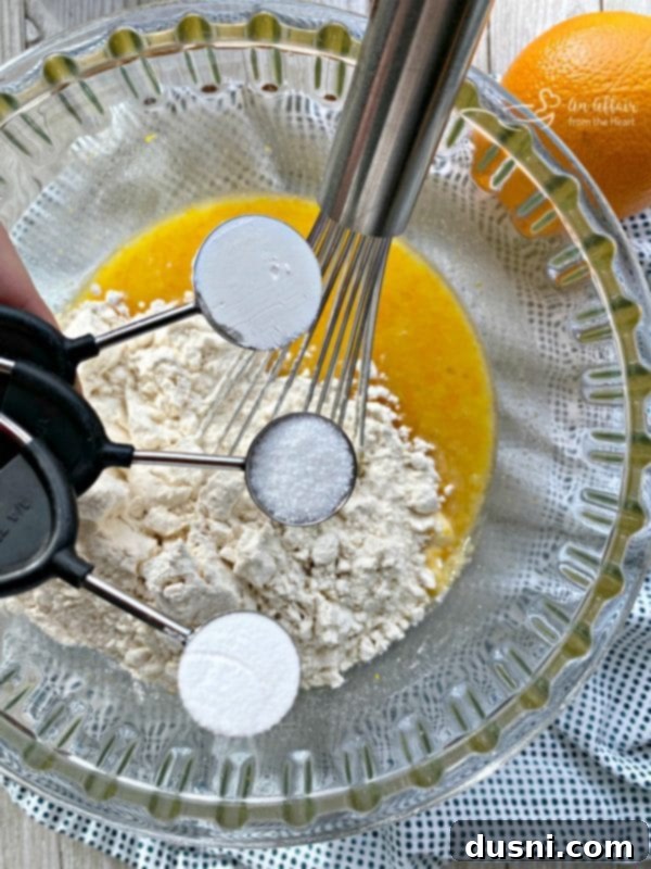 A hand whisking sugar and eggs into the wet ingredients for Blueberry Orange Bread batter.