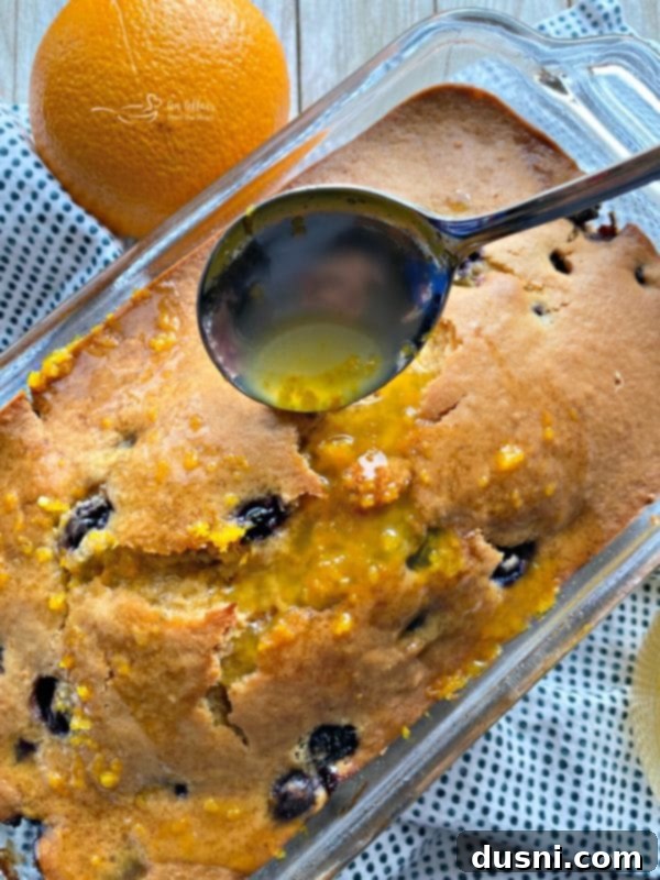Blueberry Orange Bread, still warm, with a honey-orange glaze being spooned over the top.