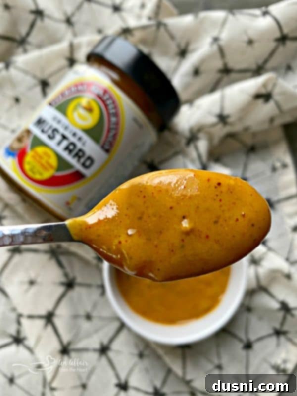 Golden Pretzel Sausage Bites with Zesty Cheese Sauce 4 A spoonful of Herbal Gatherings Original Mustard, showcasing its texture