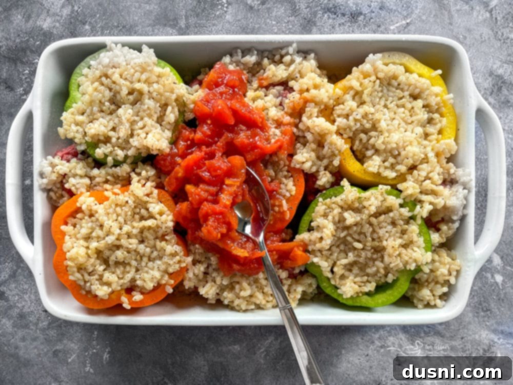 Stuffed peppers topped with rice and diced tomatoes in a baking dish, seasoned and ready.