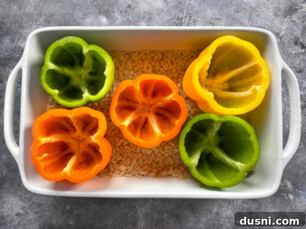 Stuffed peppers placed on a bed of rice in a baking dish, ready for filling.